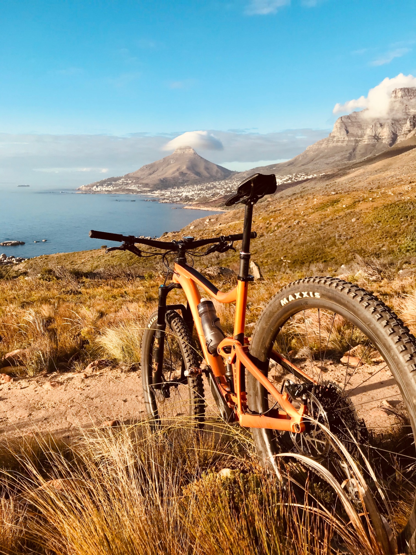 Orange full-suspension bike on a coastal hillside trail above the Atlantic